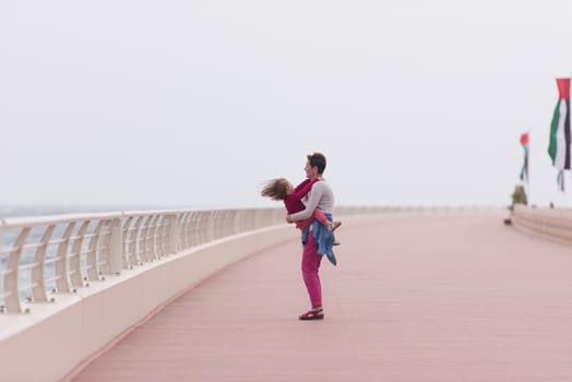 young mother and cute little girl running and cheerfully spend their time on the promenade by the sea