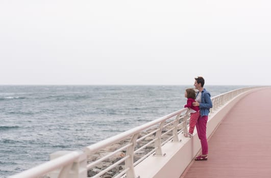 young mother and cute little girl running and cheerfully spend their time on the promenade by the sea