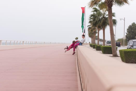 young mother and cute little girl running and cheerfully spend their time on the promenade by the sea