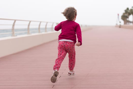 cute little girl running and cheerfully spend her time on the promenade by the sea