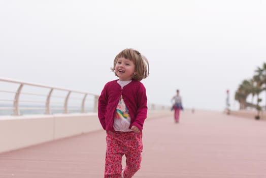 young mother and cute little girl running and cheerfully spend their time on the promenade by the sea