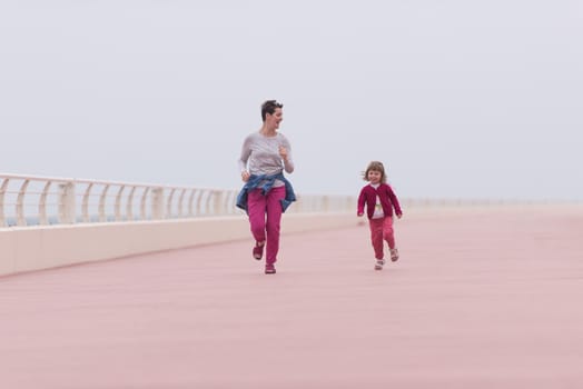 young mother and cute little girl running and cheerfully spend their time on the promenade by the sea