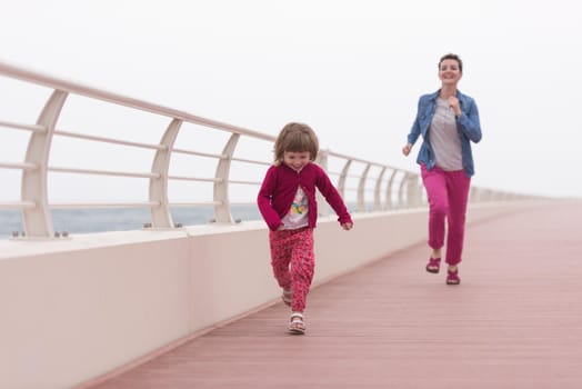 young mother and cute little girl running and cheerfully spend their time on the promenade by the sea