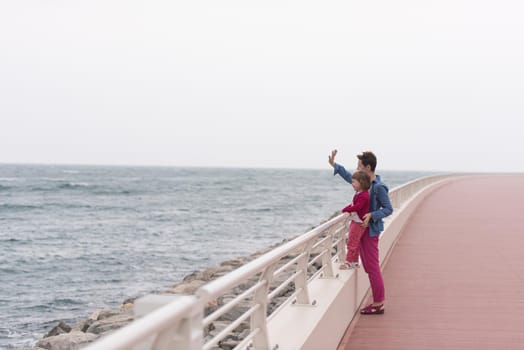 young mother and cute little girl running and cheerfully spend their time on the promenade by the sea