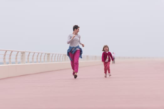 young mother and cute little girl running and cheerfully spend their time on the promenade by the sea