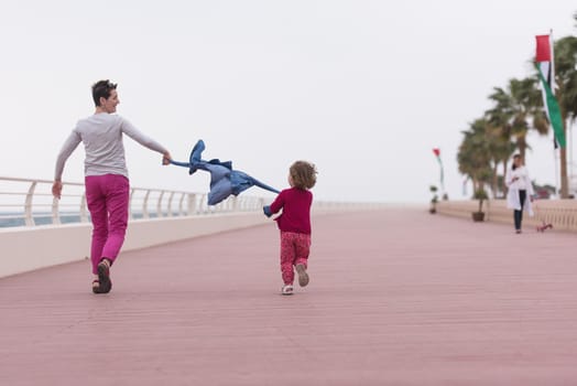 young mother and cute little girl running and cheerfully spend their time on the promenade by the sea