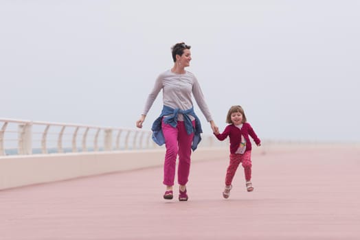 young mother and cute little girl running and cheerfully spend their time on the promenade by the sea