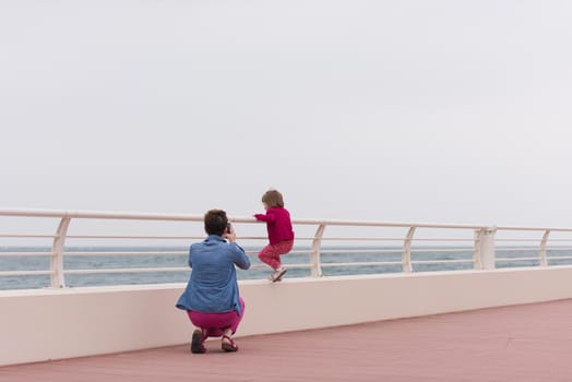 young mother and cute little girl running and cheerfully spend their time on the promenade by the sea