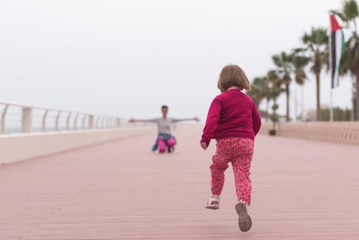 young mother and cute little girl running and cheerfully spend their time on the promenade by the sea