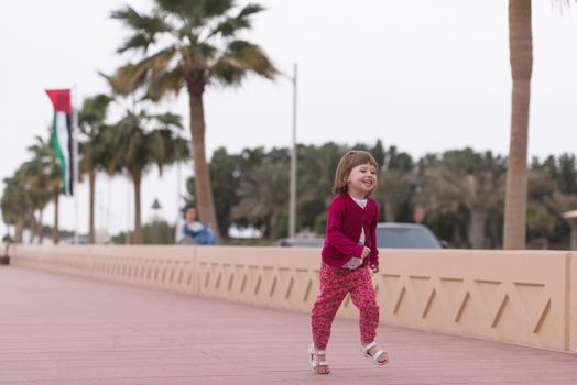 cute little girl running and cheerfully spend her time on the promenade by the sea