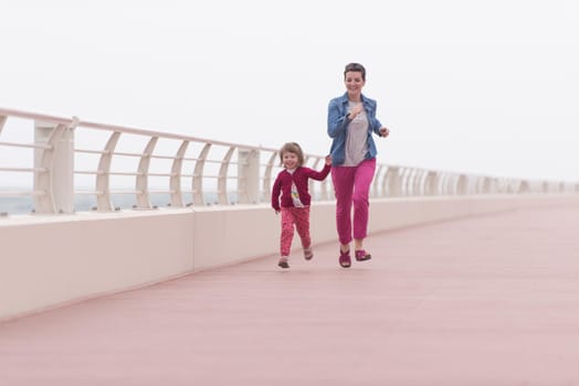 young mother and cute little girl running and cheerfully spend their time on the promenade by the sea