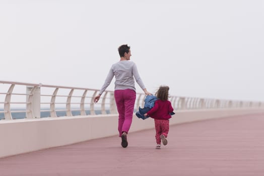 young mother and cute little girl running and cheerfully spend their time on the promenade by the sea