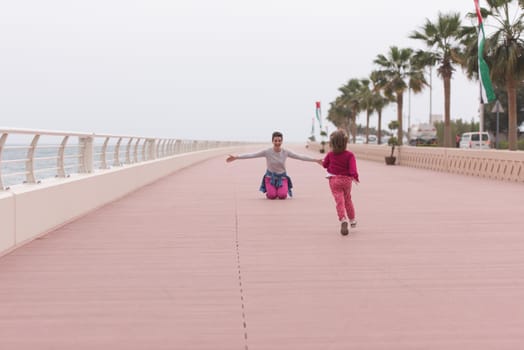 young mother and cute little girl running and cheerfully spend their time on the promenade by the sea