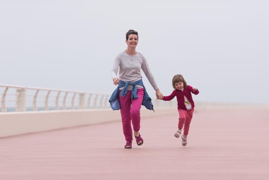 young mother and cute little girl running and cheerfully spend their time on the promenade by the sea