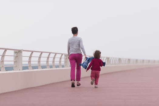 young mother and cute little girl running and cheerfully spend their time on the promenade by the sea