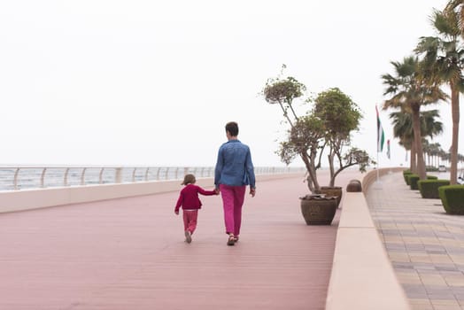 young mother and cute little girl running and cheerfully spend their time on the promenade by the sea