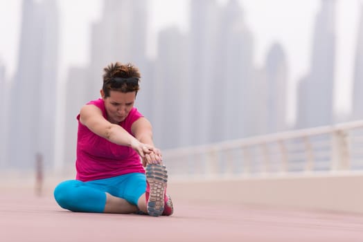 very active young beautiful woman stretching and warming up on the promenade along the ocean side with a big modern city in the background to keep up her fitness levels as much as possible