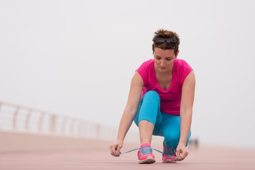 Young woman tying shoelaces on sneakers on a promenade. Standing next to a bottle of water. Exercise outdoors