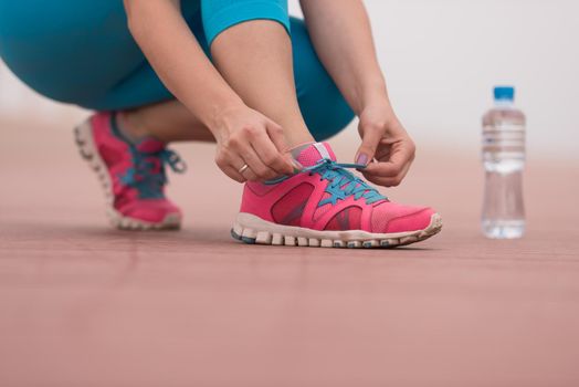 Young woman tying shoelaces on sneakers on a promenade. Standing next to a bottle of water. Exercise outdoors