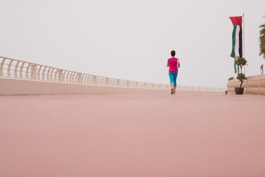 very active young beautiful woman busy running on the promenade along the ocean side to keep up her fitness levels as much as possible