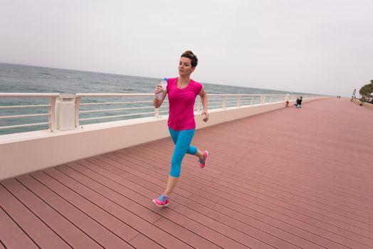 very active young beautiful woman busy running on the promenade along the ocean side to keep up her fitness levels as much as possible