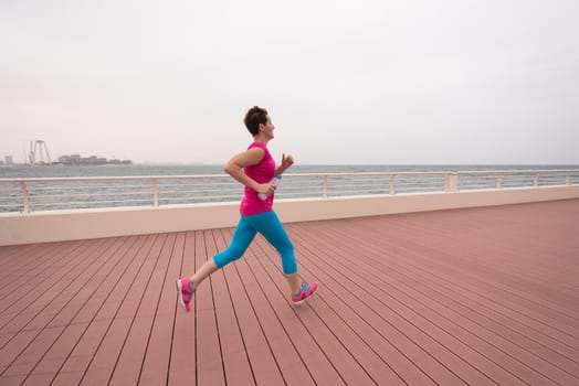 very active young beautiful woman busy running on the promenade along the ocean side with a big modern city in the background to keep up her fitness levels as much as possible