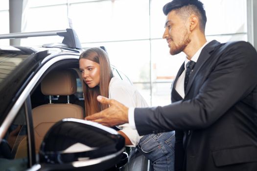 Young attractive woman looking for a new car in a car showroom