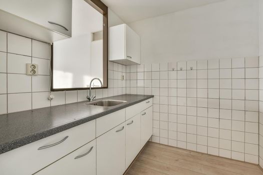 A well-organized interior of a small home kitchen with a sink under the window and light furniture in a city apartment