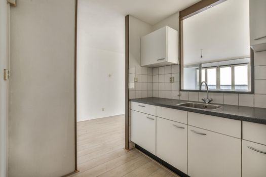 A well-organized interior of a small home kitchen with a sink under the window and light furniture in a city apartment