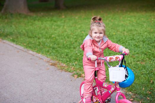 Cute smiling little girl with bicycle and helmet on road in the park