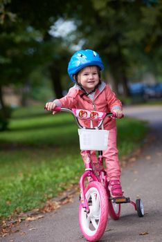 Cute smiling little girl with bicycle and helmet on road in the park