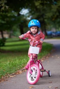 Cute smiling little girl with bicycle and helmet on road in the park