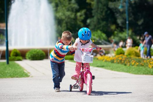 Happy childrens outdoor,  brother and sister in park have fun. Boy and girl in park learning to ride a bike.