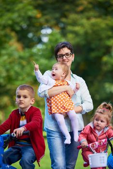 Family portrait outdoor in park. Modern mom with kids. Child learning to ride bike
