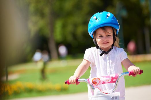 Cute smiling little girl with bicycle and helmet on road in the park