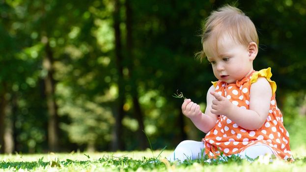 happy young baby child sittng on grass on beautiful summer day in park