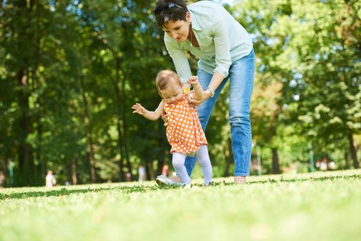 happy mother and baby child in park making first steps .  Walking and hugging.