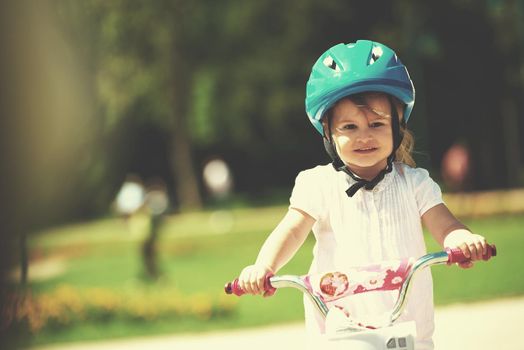 Cute smiling little girl with bicycle and helmet on road in the park