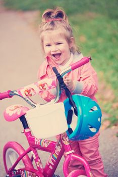 Cute smiling little girl with bicycle and helmet on road in the park