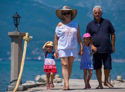 happy grandparents with cute little granddaughters having fun holding their hands while walking  by the sea during Summer vacation  Healthy family holiday concept