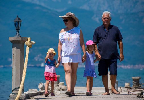 happy grandparents with cute little granddaughters having fun holding their hands while walking  by the sea during Summer vacation  Healthy family holiday concept