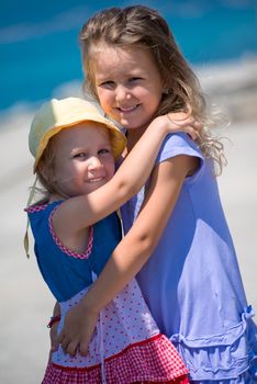 Happy smiling little sisters having fun while hugging on the beach coast during Summer vacation  Healthy childhood lifestyle concept