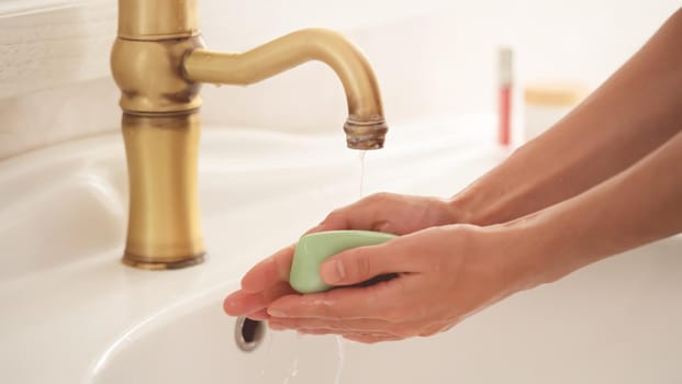 A young girl washes her hands thoroughly with soap under water in the bathroom, close-up view.