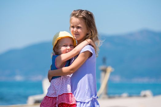 Happy smiling little sisters having fun while hugging on the beach coast during Summer vacation  Healthy childhood lifestyle concept