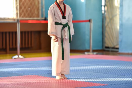 Taekwondo kids. A boy athlete stands in a taekwondo uniform with a green belt during a taekwondo tournament.