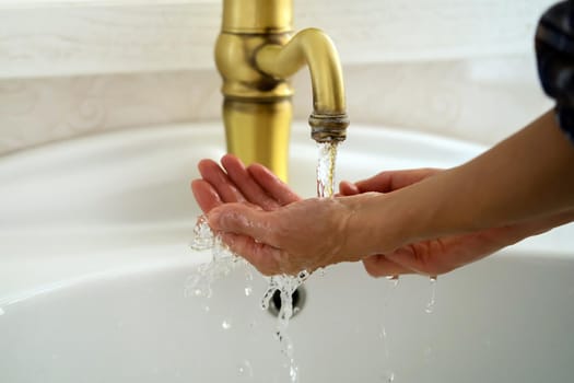 A young girl washes her hands thoroughly with soap under water in the bathroom, close-up view.