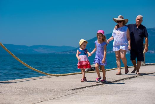 happy grandparents with cute little granddaughters having fun holding their hands while walking  by the sea during Summer vacation  Healthy family holiday concept