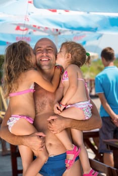 portrait of young happy father having fun with his cute little daughters while holding them in his hands by the sea during Summer vacation  Healthy family holiday concept