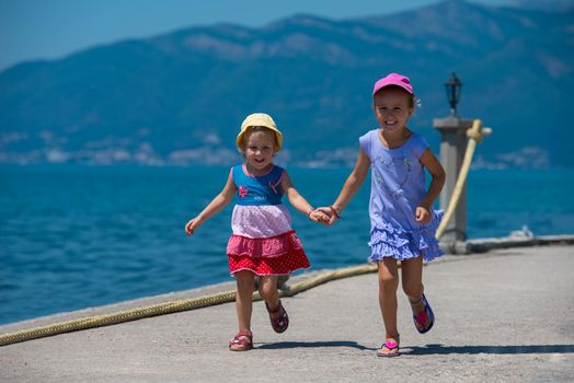 Happy smiling little sisters having fun holding their hands while running on the beach coast during Summer vacation  Healthy childhood lifestyle concept