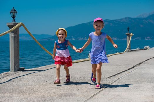 Happy smiling little sisters having fun holding their hands while running on the beach coast during Summer vacation  Healthy childhood lifestyle concept